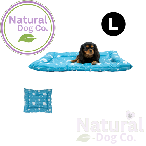 A small black and tan dog lies on a blue rectangular pet bed with a white paw print pattern. The image includes a circular 'L' size marker, a small inset of the bed's underside, and the Natural Dog Co.